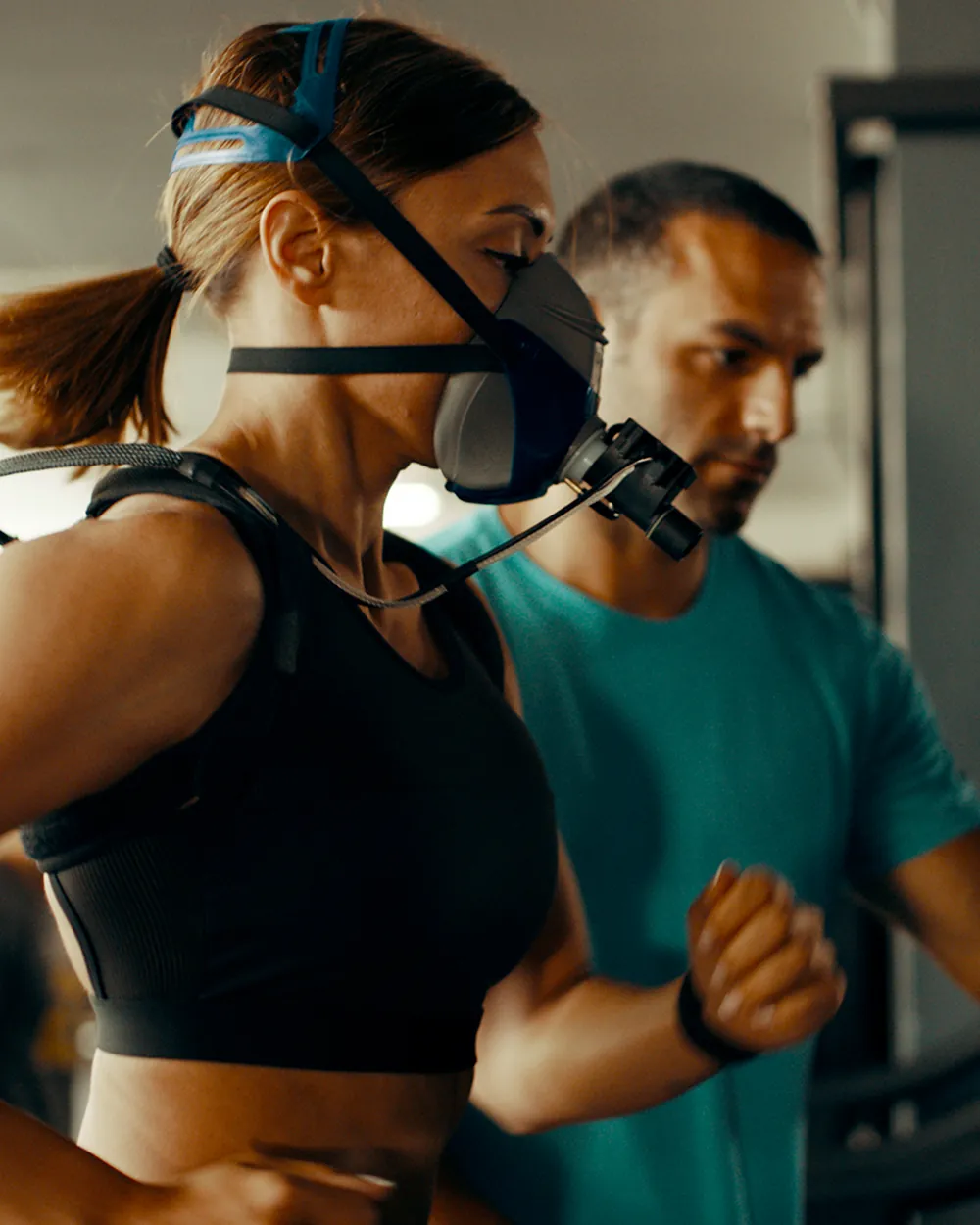 An athlete running on a treadmill wearing a metabolic analysis mask while a technician monitors the test.